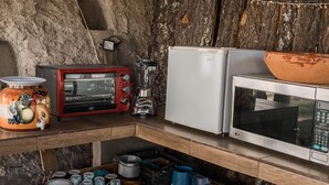 Una cocina rústica con pared de piedra, repisa de madera con electrodomésticos y una variedad de platos y utensilios.