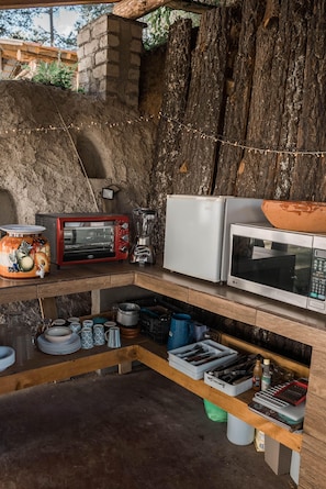 Una cocina rústica con pared de piedra, repisa de madera con electrodomésticos y una variedad de platos y utensilios.