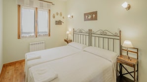 A double bed with a wooden headboard, a bedside table with a lamp, a window with curtains, and wall decor. - Country House 'La Cardeñuela' with Mountain View, Private Terrace and Wi-Fi (Burgos)