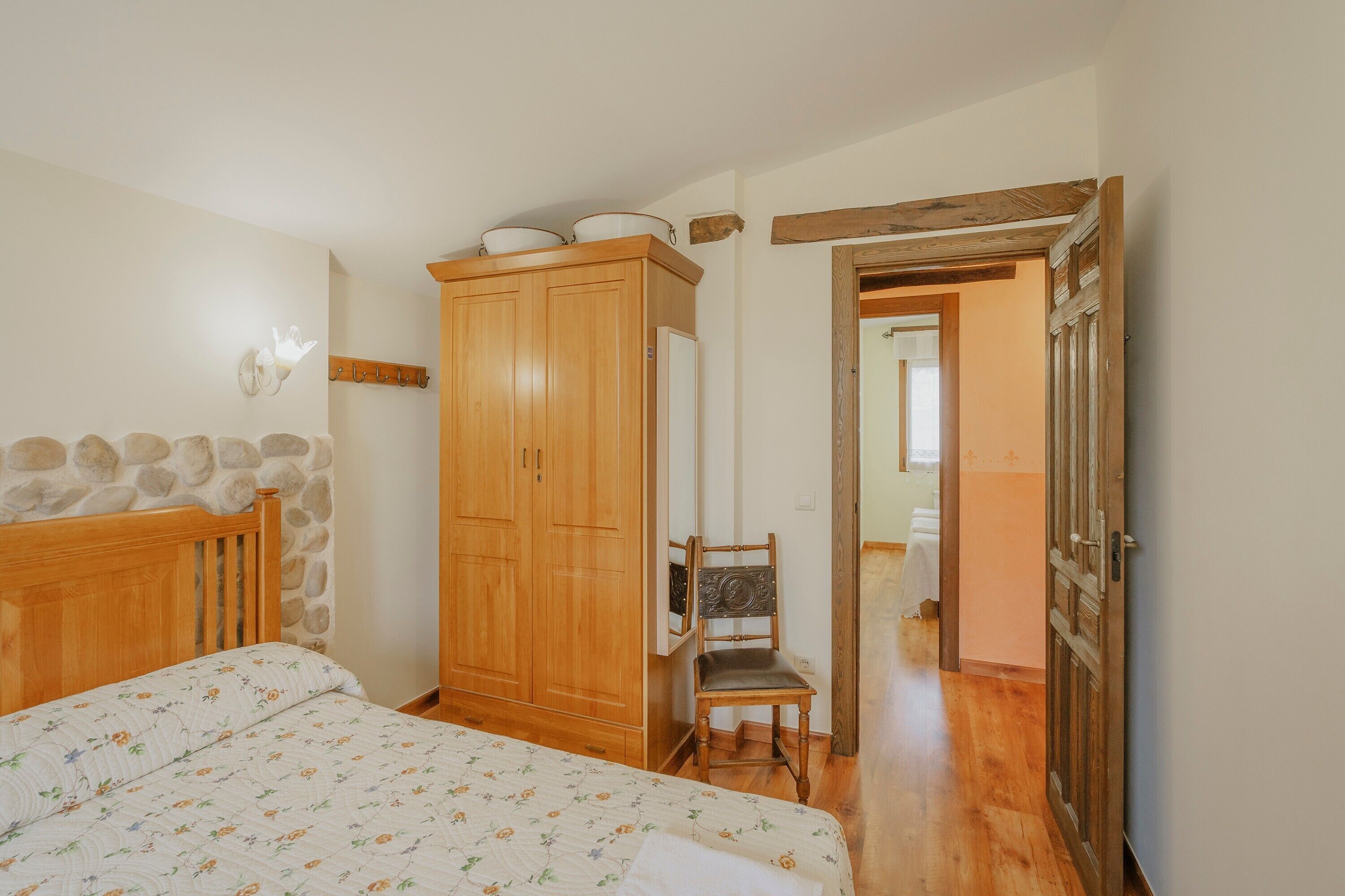 Un dormitorio con cama, armario de madera, silla y pared de piedra.