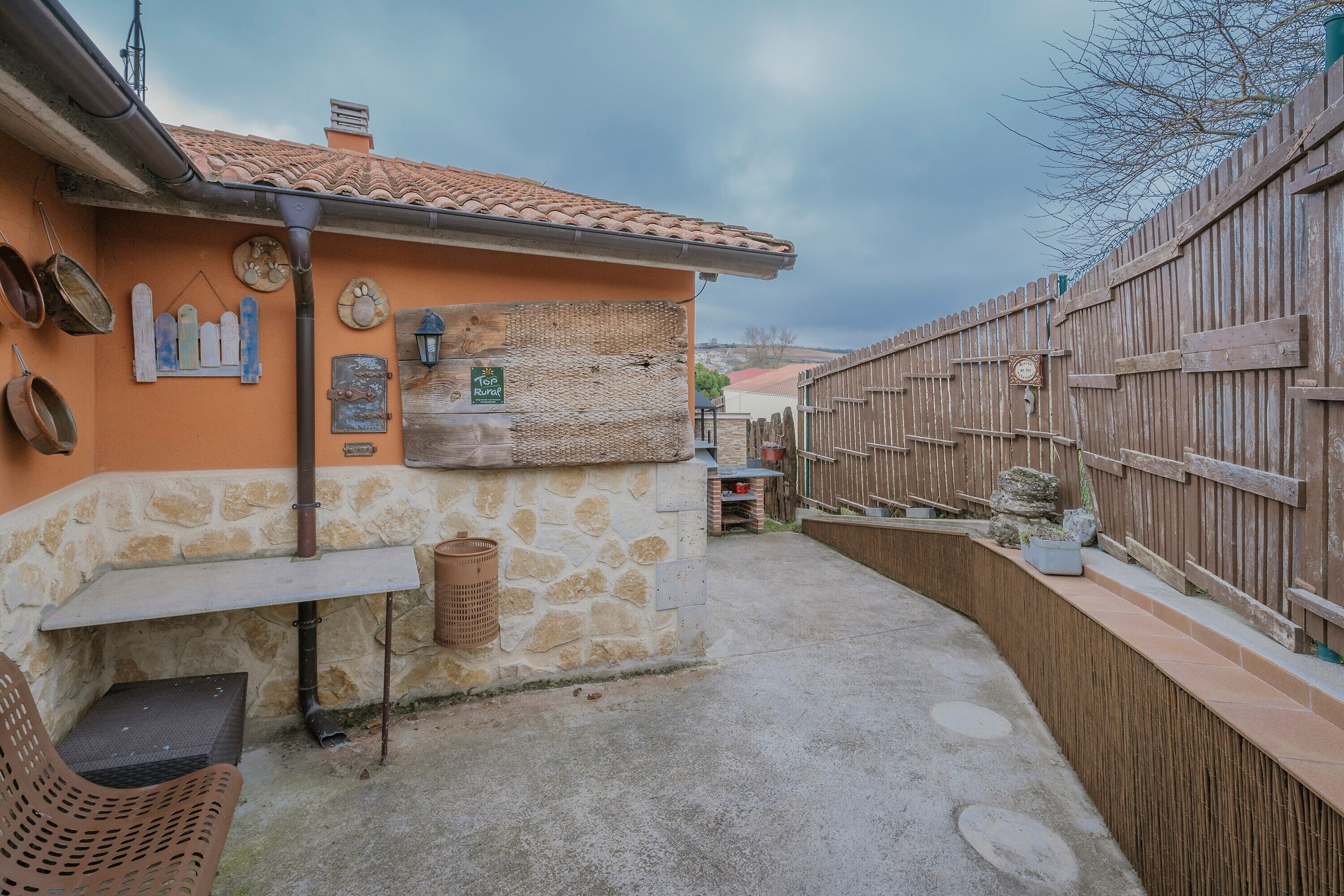 A rustic outdoor patio with stone walls, a wooden fence, and a small table with a chair.