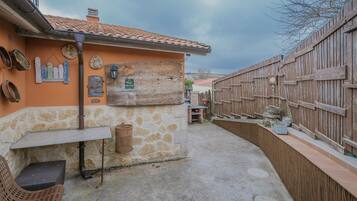 A rustic outdoor patio with stone walls, a wooden fence, and a small table with a chair.