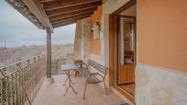 A balcony with a wooden pergola, a stone wall, a bench, and a table. - Country House 'La Cardeñuela' with Mountain View, Private Terrace and Wi-Fi (Burgos)