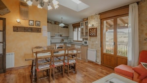 A spacious living area with a dining table and chairs, a sofa, a coffee table, and a view through a large sliding glass door. - Country House 'La Cardeñuela' with Mountain View, Private Terrace and Wi-Fi (Burgos)