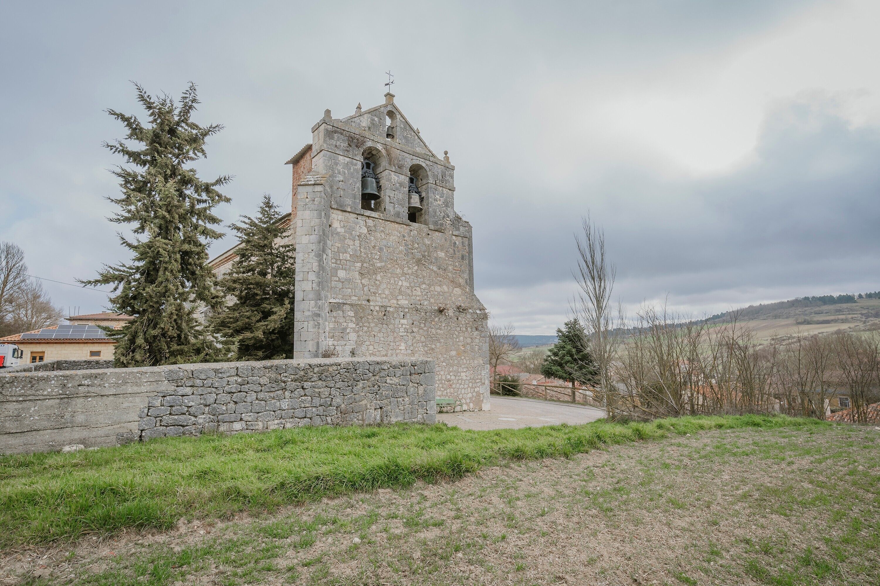 Església de pedra amb un campanar, envoltada d'herba i arbres.