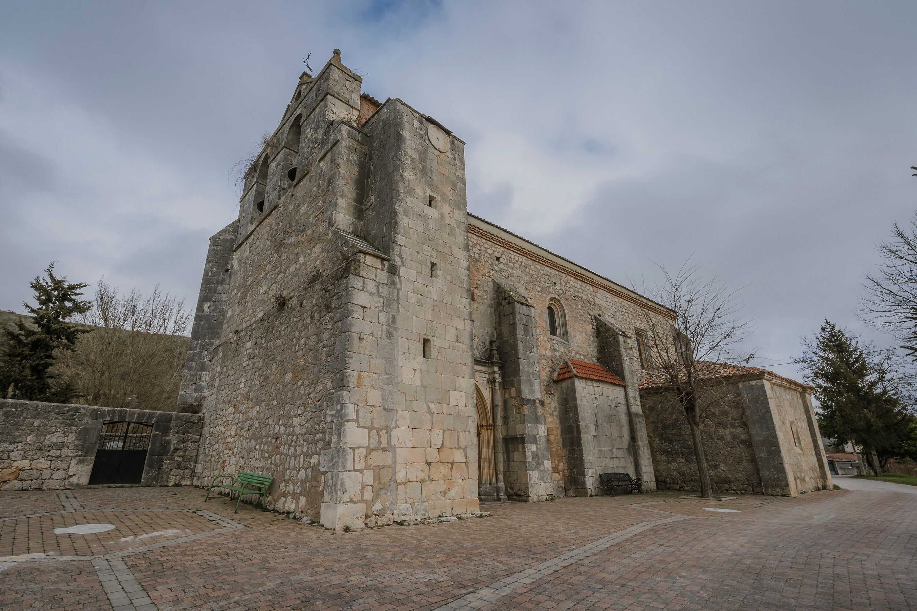 A historic stone building with a tower, a gated entrance, and a paved courtyard.