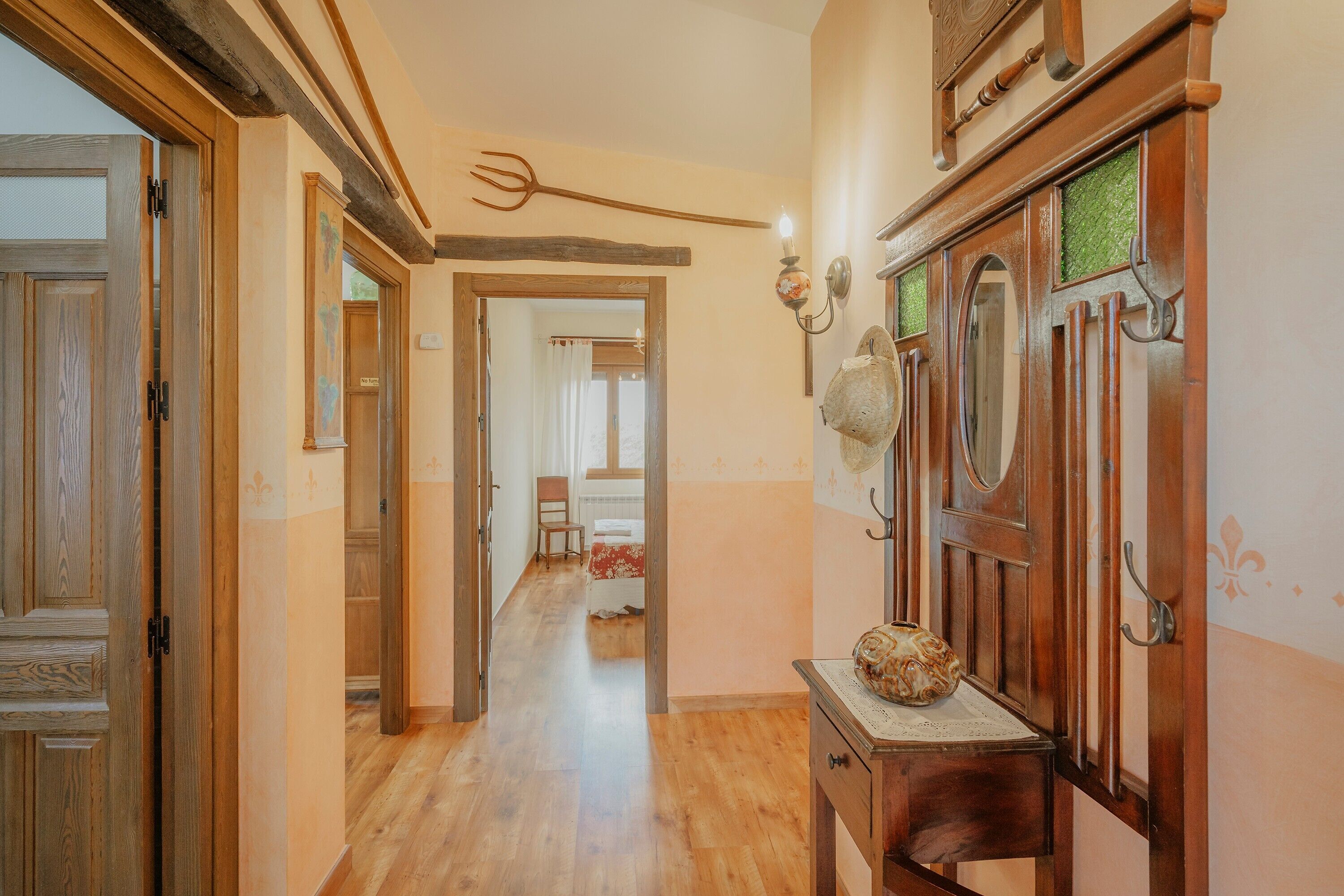 Un couloir avec des portes en bois, une table en bois surmontée d’un vase et un luminaire fixé au mur.