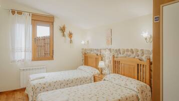A bedroom with two beds, a window with a curtain, a radiator, a stone wall, and a wooden headboard.