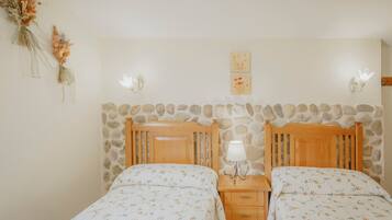 Un dormitorio con dos camas, cabecero de madera, mesita de noche con lámpara y pared de piedra.
