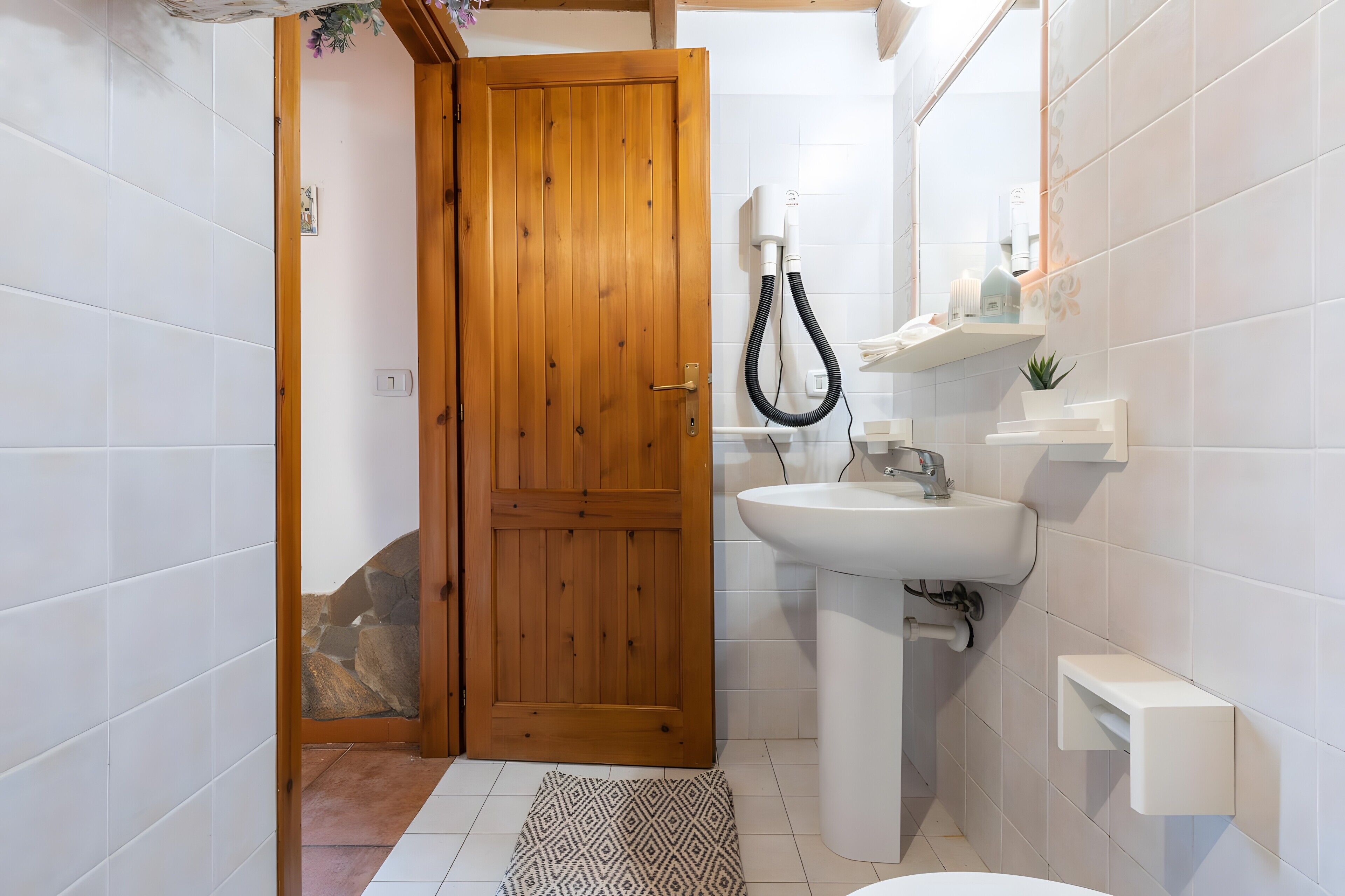 A bathroom with a wooden door, a white sink, and a shower area.