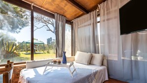 Een slaapkamer met een bed, een televisie, een raam met gordijnen en uitzicht op een tuin.