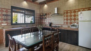 Uma cozinha com uma mesa de jantar, cadeiras, geladeira e uma janela com persianas.