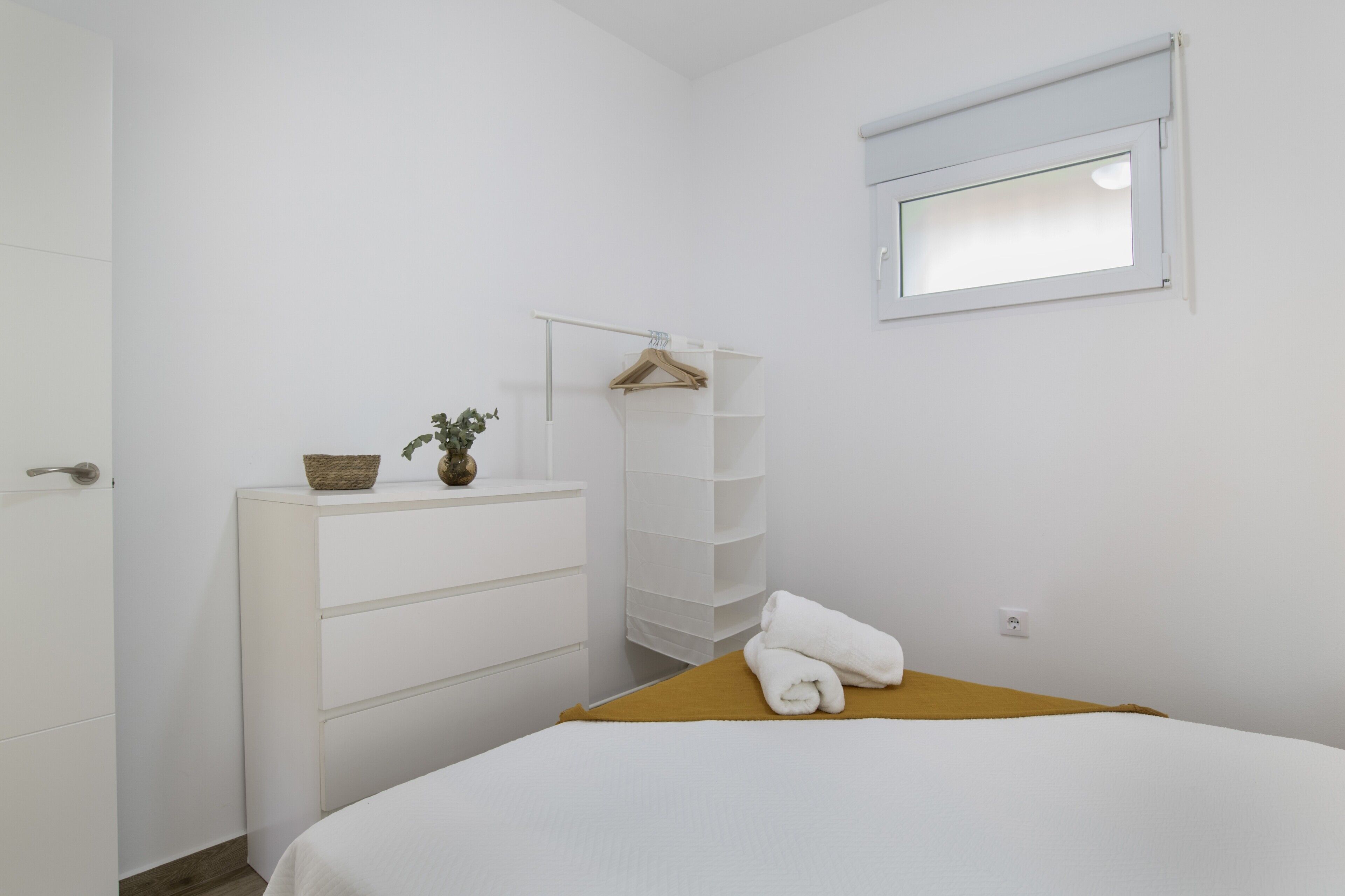 Een slaapkamer met een bed, een dressoir, een wandplank, een raam en een deur.