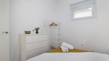 Een slaapkamer met een bed, een dressoir, een wandplank, een raam en een deur.