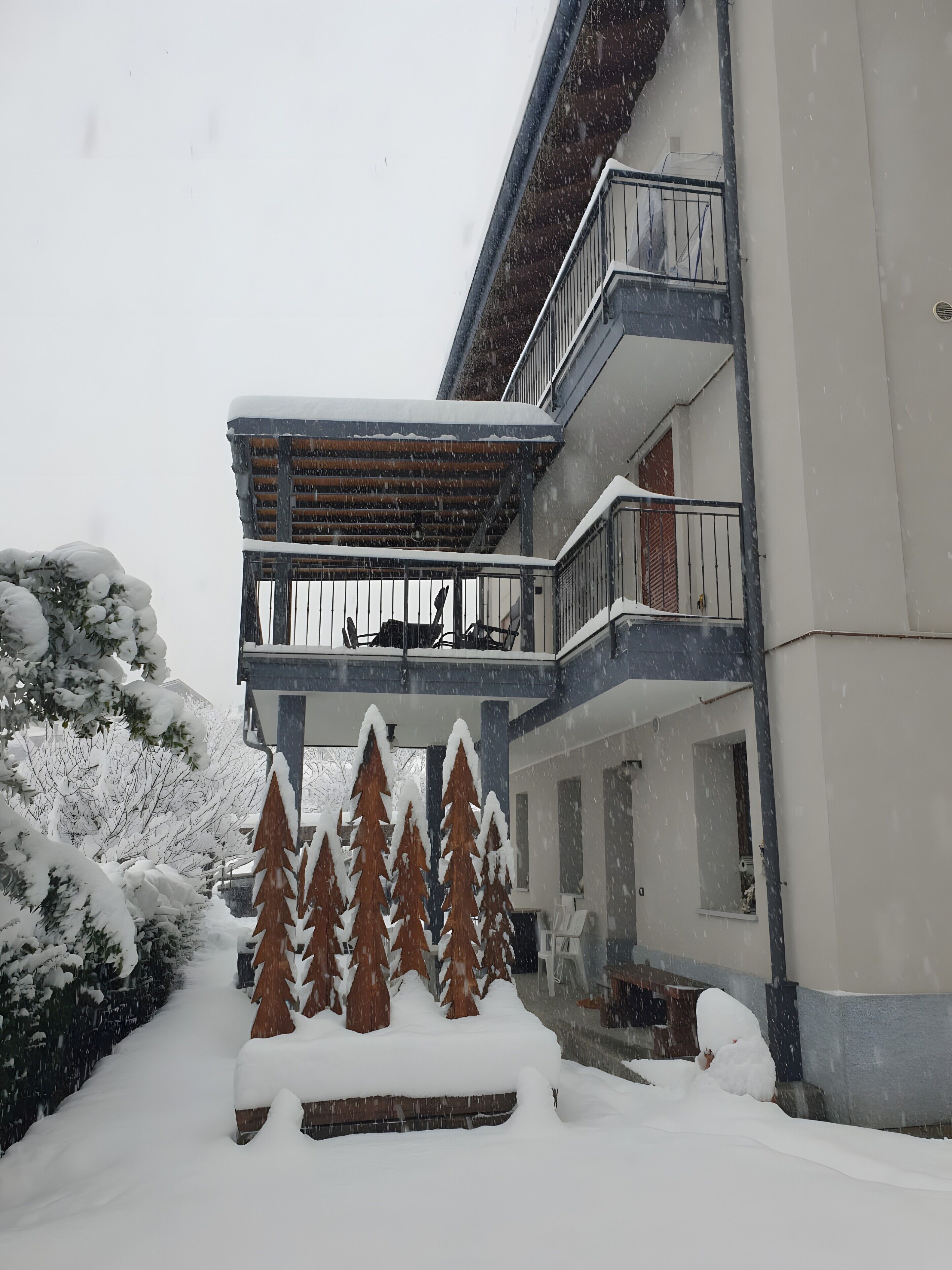 Un immeuble à plusieurs étages doté d’un balcon, des arbres couverts de neige et un sol enneigé.