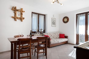 Uma sala de jantar com mesa de madeira, cadeiras e um sofá com almofada vermelha.