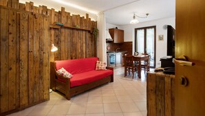 Un espace de vie compact avec un séparateur en bois, un canapé rouge, un coin repas et une petite cuisine.