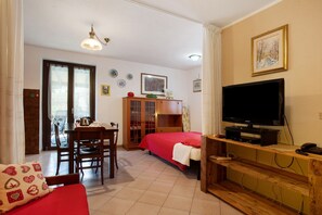 A room with a bed, a TV, a wooden cabinet, a dining table with chairs, and a window with curtains. - Studio 'A4 Piano Rialzato' with Mountain View, Private Terrace and Wi-Fi (Saint Pierre)