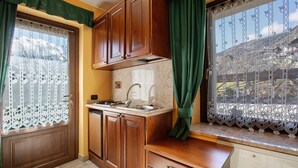 Une cuisine de taille réduite, dotée de meubles de rangement en bois, d’un plan de travail et d’une fenêtre agrémentée d’un rideau décoratif.