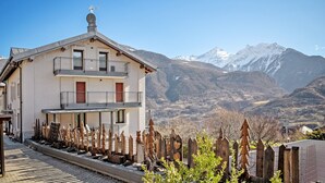 Un bâtiment à deux étages doté d’un balcon, d’une clôture en bois et ayant une chaîne de montagnes en arrière-plan.
