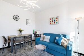 A modern living room with a blue sofa, a dining table with chairs, a small round table with a tray, and a floor lamp.