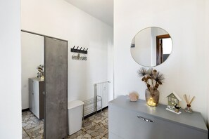 Un bagno moderno con un mobile grigio, uno specchio rotondo, un cartello con la scritta 'welcome', un termosifone e una piccola decorazione a forma di casetta sul ripiano.