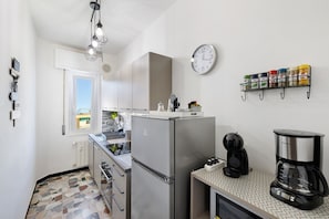 A compact kitchen with a refrigerator, coffee maker, and spice rack.