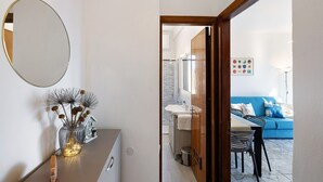 A modern interior with a mirror, a vase with dried flowers, a small house-shaped decoration, a dining area with a table and chairs, and a blue sofa with a colorful wall art piece. - Apartment 'Vista Mare A 150 Mt Dalla Spiaggia' with Sea View, Private Terrace and Air Conditioning (Pietra Ligure)