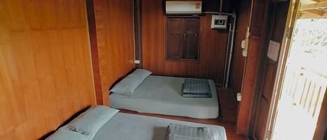 A cabin interior with two beds, wooden walls, a ceiling fan, and a window with a view.