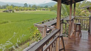 A wooden deck with a view of a green field and distant mountains. - hueankwankhao  (Chom Thong)