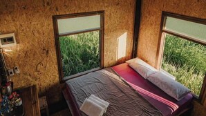 A single bed with a red and white striped bedspread in a rustic room with wooden walls and large windows. - hueankwankhao  (Chom Thong)