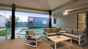 A covered outdoor seating area with a pool, a sofa, and a chair. - 6 Dooley Street Bargara (Bargara)