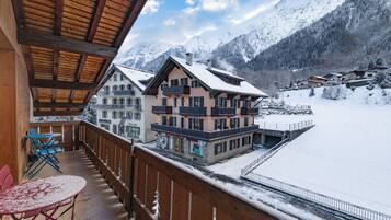 Ein Balkon mit Blick auf schneebedeckte Berge, eine Holzterrasse und ein Tisch mit Stühlen.
