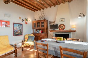 Una zona pranzo con tavolo apparecchiato per due, un mobiletto in legno con libri, una televisione e decorazioni alle pareti.
