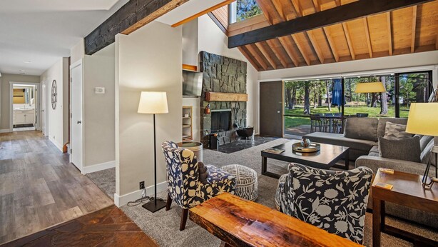 A spacious living area with a high ceiling, a fireplace, and a large window overlooking a garden. - Cozy Condo Near the VIllage (Sunriver)