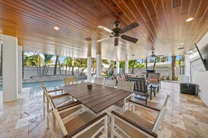 Eine Terrasse im Freien mit Holzboden, einem Pool und einer Essgegend mit Stühlen und Tisch.