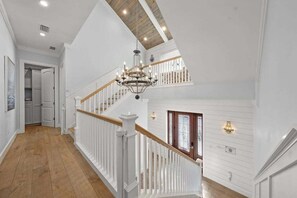 A spacious interior with a wooden staircase, a chandelier, and a view of a kitchen.