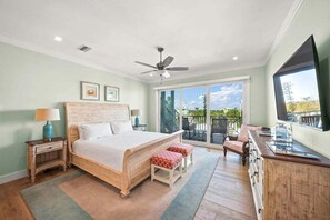 Ein Schlafzimmer mit Bett, Deckenventilator, Nachttisch, Kommode, Fernseher und einem Balkon mit Blick.