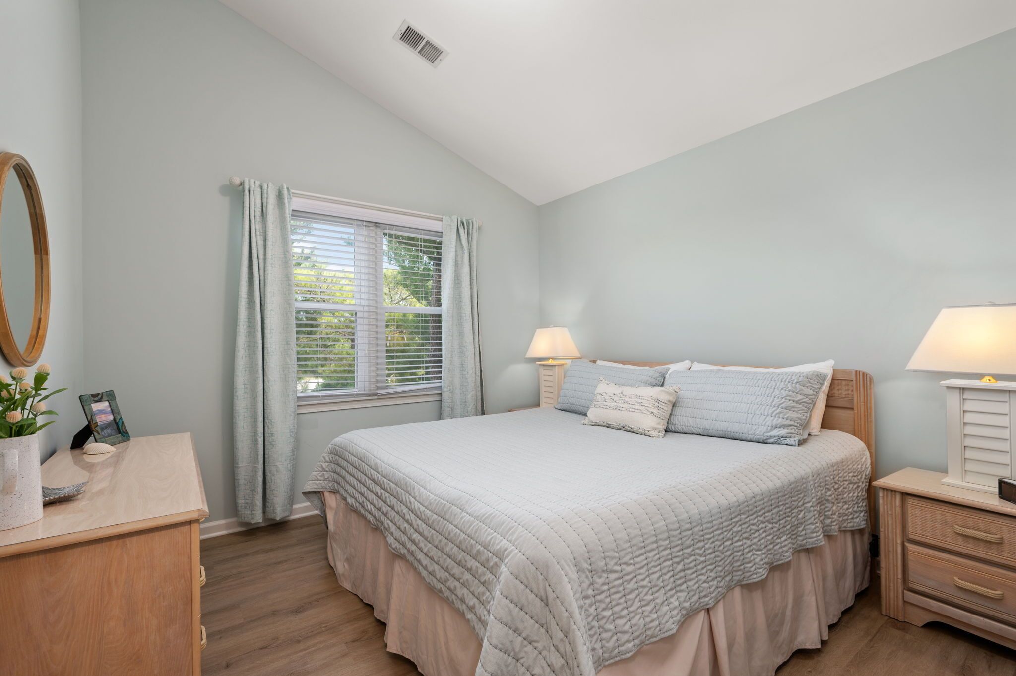 Une chambre à coucher avec un lit, des lampes de chevet, une commode, un miroir et une fenêtre avec des rideaux.