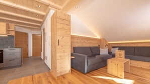Un interior moderno con vigas de madera, un sofá gris, una mesa de centro de madera y una zona de cocina.