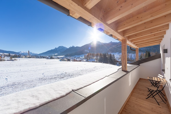 A wooden balcony with a view of a snowy landscape and mountains.