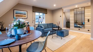 A modern living room with a dining area, a blue sofa, a round table, and a large mirror. - F27 Living Whg. 08 - F27 Living (Sylt)
