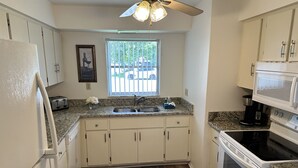A kitchen with white cabinets, a granite countertop, a built-in oven, a microwave, and a ceiling fan. - Peaceful Cottage, your perfect getaway in the Cape (Cape Coral)