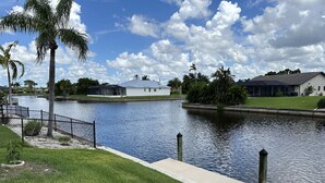 A calm waterway with a grassy bank, a fence, and a row of houses in the background. - Peaceful Cottage, your perfect getaway in the Cape (Cape Coral)