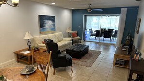 A living room with a sofa, a coffee table, a dining table with chairs, a TV, and a large window. - Peaceful Cottage, your perfect getaway in the Cape (Cape Coral)
