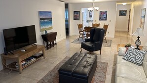 A living room with a TV, leather sofa, and a dining area with chairs and a table. - Peaceful Cottage, your perfect getaway in the Cape (Cape Coral)
