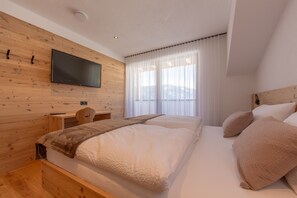 Une chambre avec un mur en bois, un téléviseur à écran plat, un lit avec une literie blanche et une fenêtre ornée de rideaux légers.