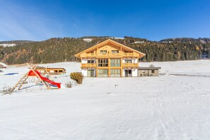 Un chalet avec une façade en bois, un balcon et un toboggan rouge, le tout situé dans un paysage enneigé.