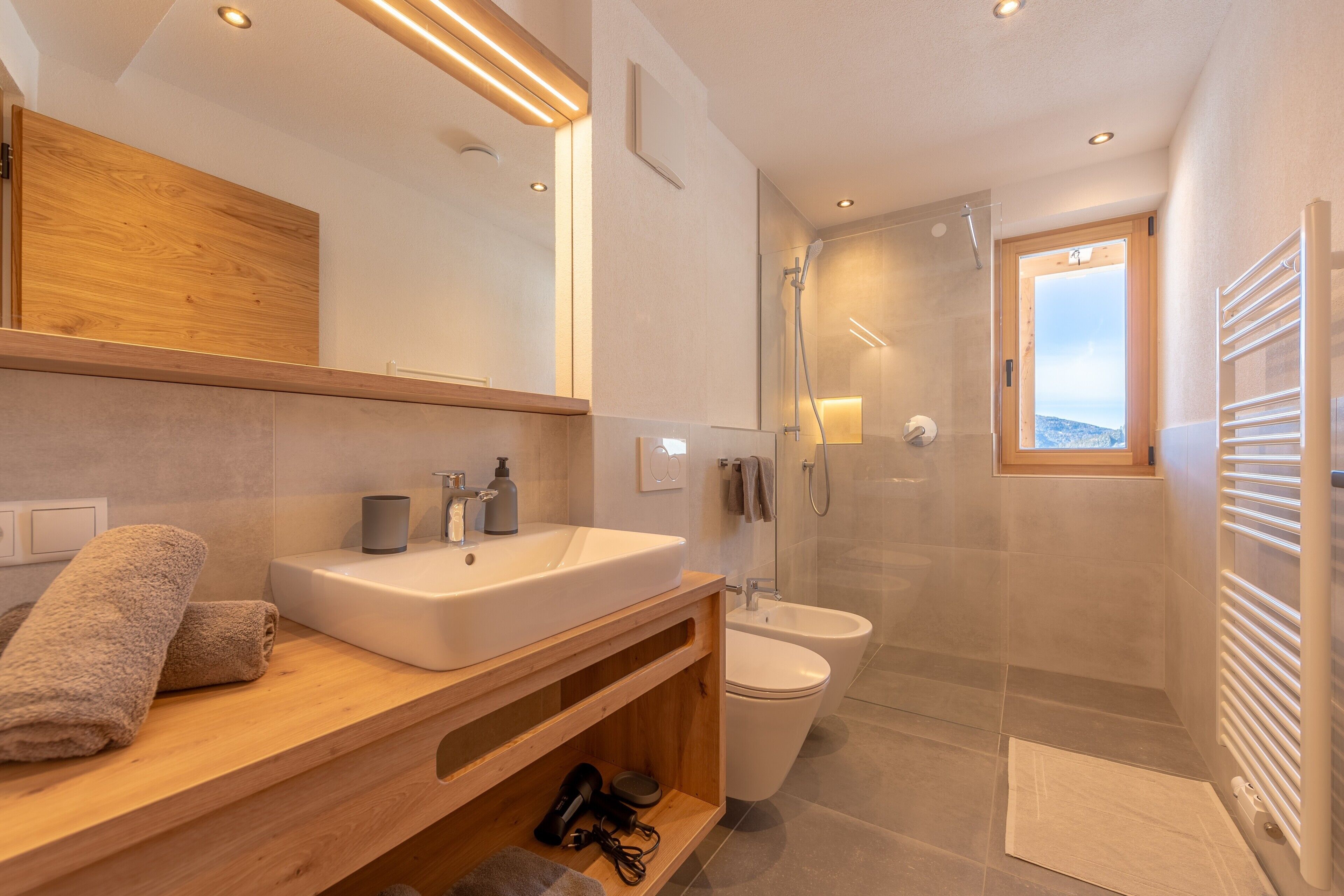 Une salle de bain moderne avec un meuble-lavabo en bois, un grand miroir, une cabine de douche et une vue à travers la porte de la douche.