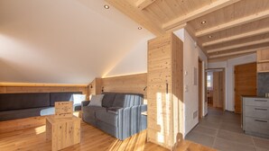 Et moderne loftværelse med træloft, en grå sofa, et træbord og et køkken med grå skab.
